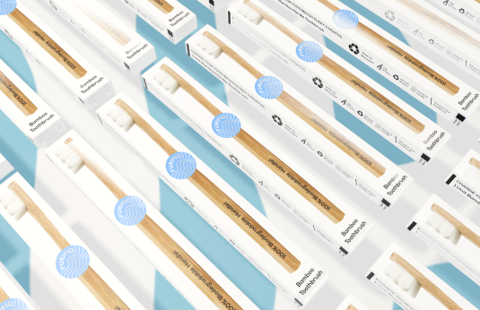 A couple of Purifiq Bamboo Toothbrush in packaging placed against a flavorful blue and white studio background.